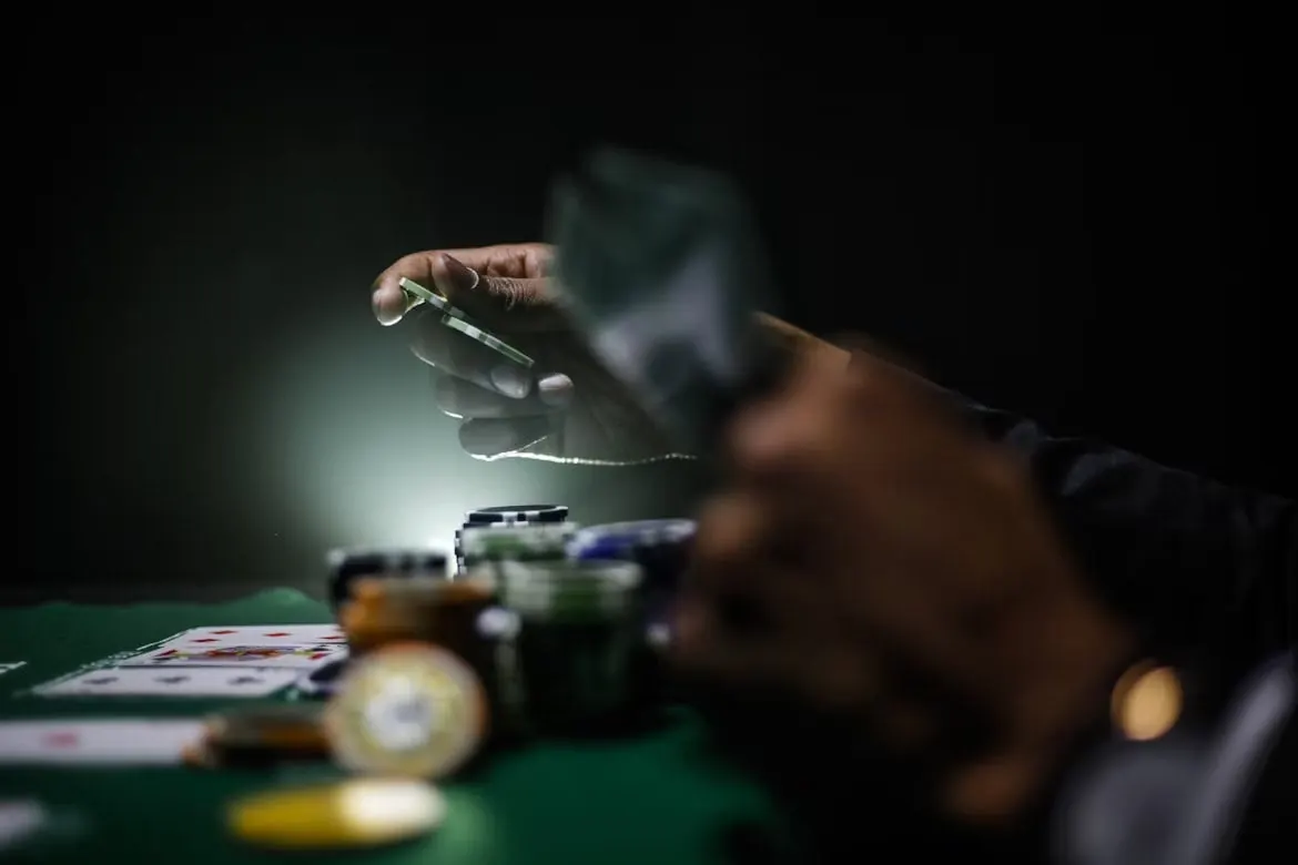 La mano de un jugador sosteniendo una ficha de póker sobre pilas en una mesa oscura evoca la tensión y riesgos del uso de soluciones de póker con bots