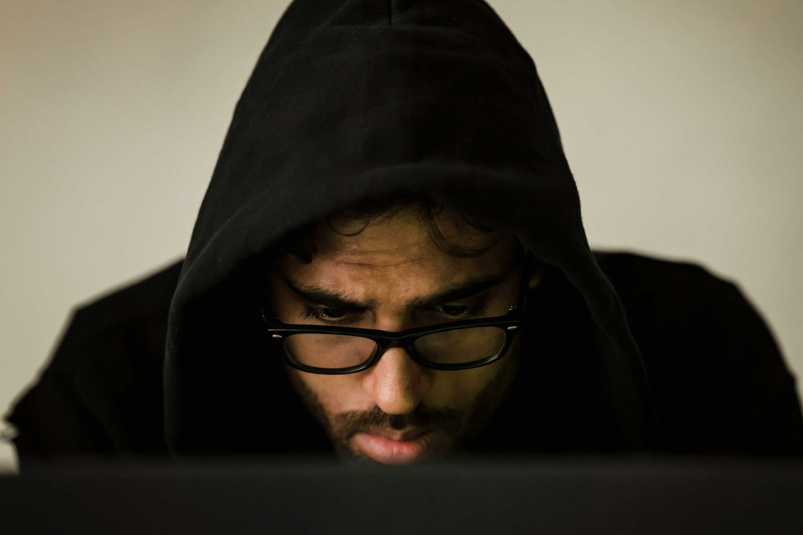 Usuário encapuzado em um laptop, ilustrando os riscos do mercado cinza em Assistentes de Poker com IA