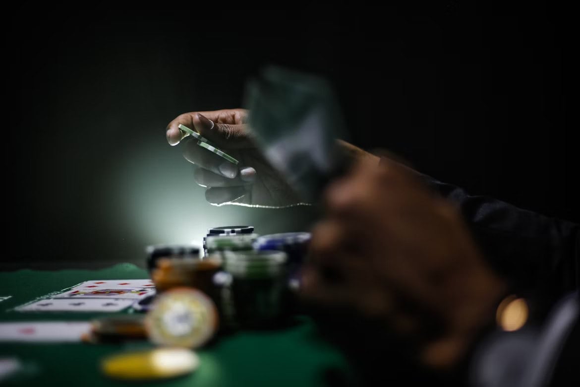 A player’s hand holding a poker chip above stacks on a dark table evokes the suspense and risks of using bot poker solutions
